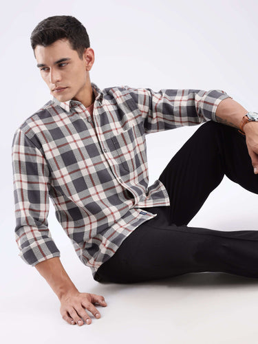 Man seated wearing a grey checked shirt made from recycled cotton, showcasing sustainable style and comfort.