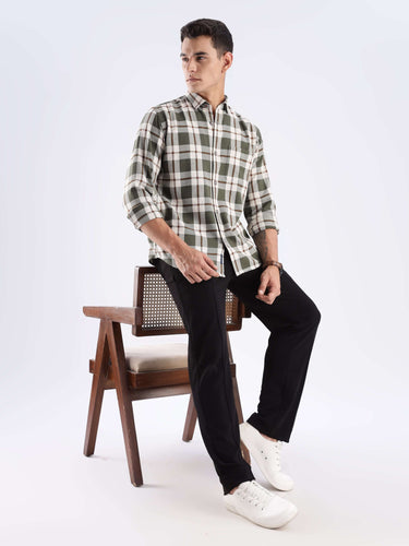Man wearing a Meteor Green checked shirt made from recycled cotton, seated casually on a chair.
